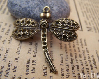 May include: A bronze dragonfly charm with intricate details. The wings are decorated with a pattern of small circles and the body is long and slender.