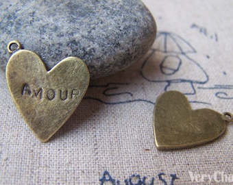 May include: Two antique gold-tone heart-shaped charms. One charm has the word "AMOUR" engraved on it.