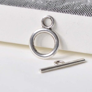 Può includere: Chiusura a scatto in metallo argentato con un anello rotondo e una barra dritta. La chiusura è utilizzata per la creazione di gioielli.