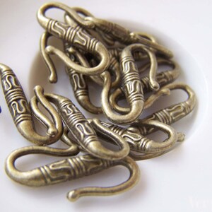 May include: A close-up of a pile of antique gold-toned metal hooks with intricate designs. The hooks are all the same size and shape, and they are arranged in a random pattern.