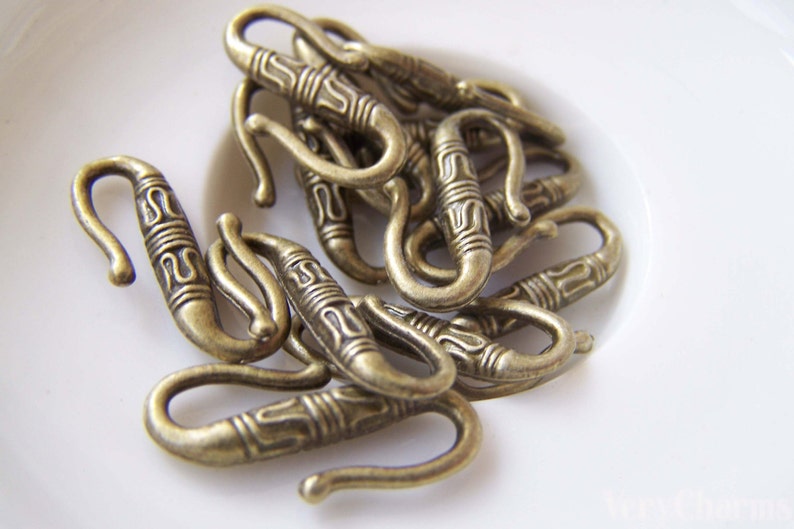 May include: A close-up of a pile of antique gold-toned metal hooks with intricate designs. The hooks are all the same size and shape, and they are arranged in a random pattern.