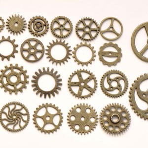 Pode incluir: Uma coleção de 20 engrenagens de metal dourado antigo de vários tamanhos e designs. As engrenagens estão dispostas em filas sobre um fundo branco.