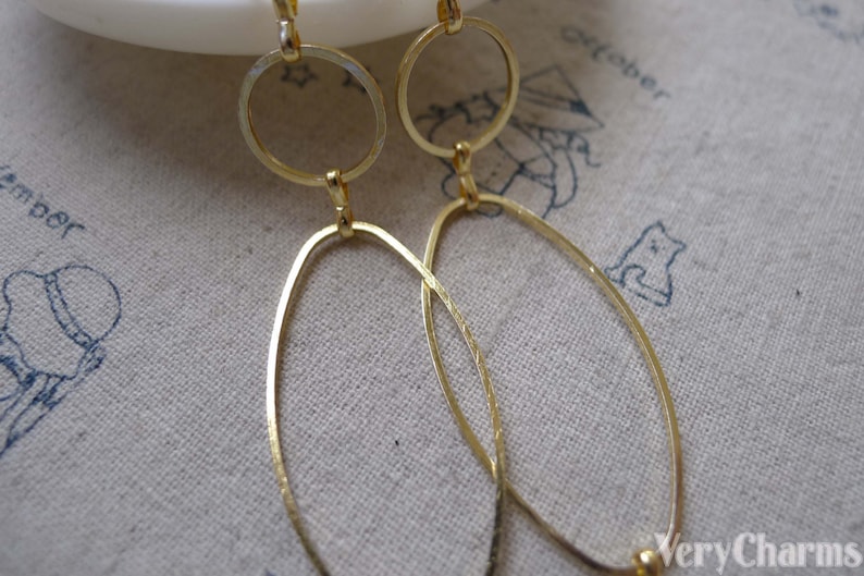 May include: A pair of gold-toned dangle earrings with two oval shapes and a smaller circle on each earring.