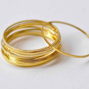 Può includere: Un set di sette braccialetti in metallo color oro. I braccialetti sono tutti della stessa dimensione e sono impilati uno sopra l'altro. Un braccialetto è posto accanto alla pila.