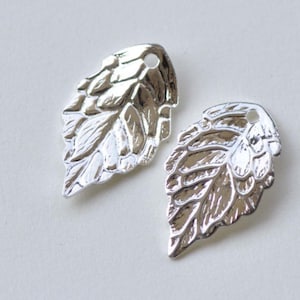 May include: Two silver leaf-shaped charms with a hole at the top for attaching to jewelry or other crafts.