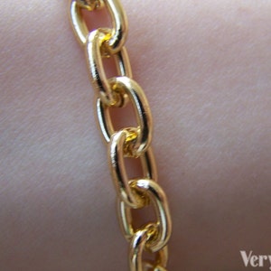 May include: A close-up of a gold chain necklace with a curb link style. The chain is smooth and shiny.