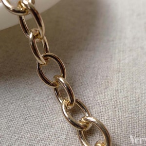 May include: Close-up of a gold-colored chain with oval links. The chain is made of metal and has a shiny finish. The chain is on a light-colored surface.