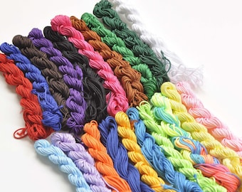 May include: A collection of colorful braided cords in various shades, including red, pink, green, and blue. The cords are arranged diagonally against a white background, showcasing a variety of crafting supplies.