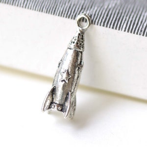May include: Silver-toned rocket ship charm with a star on the side. The charm has a loop at the top for attaching to a necklace or bracelet.
