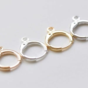 May include: Four earring hoops in different finishes: gold, silver, rose gold, and a darker gold. The hoops are open and have a hinged clasp.