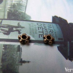 May include: Two antique gold-toned metal bead caps with a round hole in the center. The bead caps are on a white surface with a blurred background.