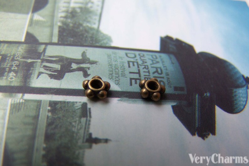 May include: Two antique gold-toned metal bead caps with a round hole in the center. The bead caps are on a white surface with a blurred background.