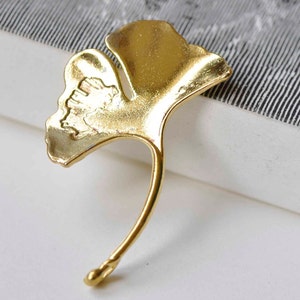 Peut inclure: Un charme en forme de feuille de ginkgo de couleur dorée avec un design détaillé. La feuille est incurvée et possède une tige.
