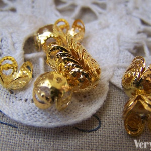 May include: Gold metal bead caps with a decorative, intricate design. The caps are small and have a delicate, filigree look.