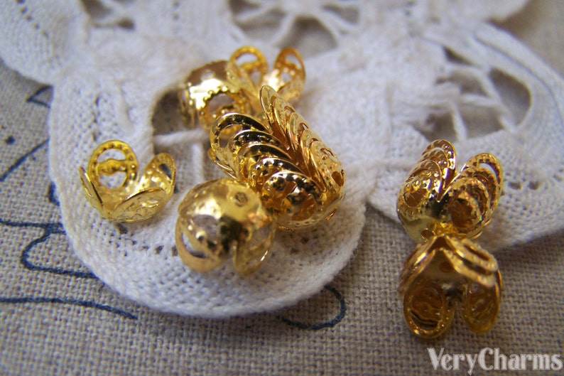 May include: Gold metal bead caps with a decorative, intricate design. The caps are small and have a delicate, filigree look.
