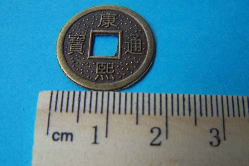 K&ouml;nnte beinhalten: Eine bronzene chinesische M&uuml;nze mit einem quadratischen Loch in der Mitte. Die M&uuml;nze tr&auml;gt chinesische Schriftzeichen, darunter "Wohlstand" und "Gl&uuml;ck". Die M&uuml;nze hat einen Durchmesser von etwa 2,5 cm.