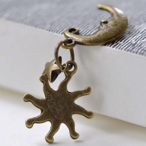 May include: A bronze charm with a crescent moon and a star-shaped sun. The charm is attached to a ring.