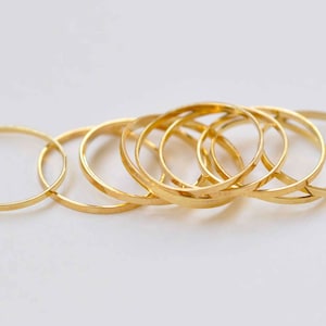 Può includere: Una collezione di anelli sottili e delicati in oro disposti su una superficie bianca. Gli anelli sono circolari e sembrano essere fatti di un metallo lucido e lucido. Gli anelli sono di diverse dimensioni e si sovrappongono leggermente.