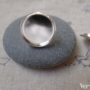May include: Two silver earring blanks with round, flat, silver-toned metal bases. The bases are smooth and have a slight curve to them. The earring posts are attached to the back of the bases.