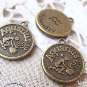 May include: Three bronze-colored metal charms with the zodiac sign Aquarius. The charms are round and have a raised design of the Aquarius symbol and the word "Aquarius" written around the edge. One charm has the word "Friendly" written on the back.