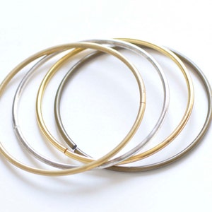 May include: Four gold, silver, and bronze bangle bracelets stacked together. The bracelets are all simple and circular.