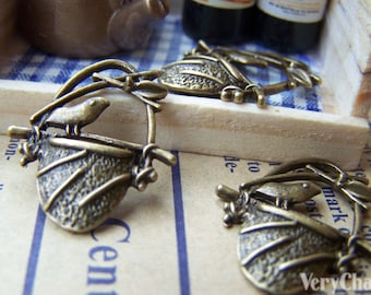 May include: Two antique gold-toned metal charms featuring a bird perched on a small pot. The charms are detailed with intricate designs and have a rustic, vintage aesthetic.
