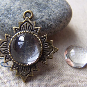 May include: A bronze pendant with a clear glass cabochon in the center. The pendant is shaped like a star with intricate details. A smaller clear glass cabochon is also shown in the image.