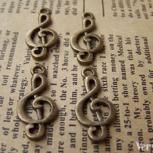 May include: Five antique gold-toned treble clef charms. The charms are arranged in a row on a piece of paper with text.