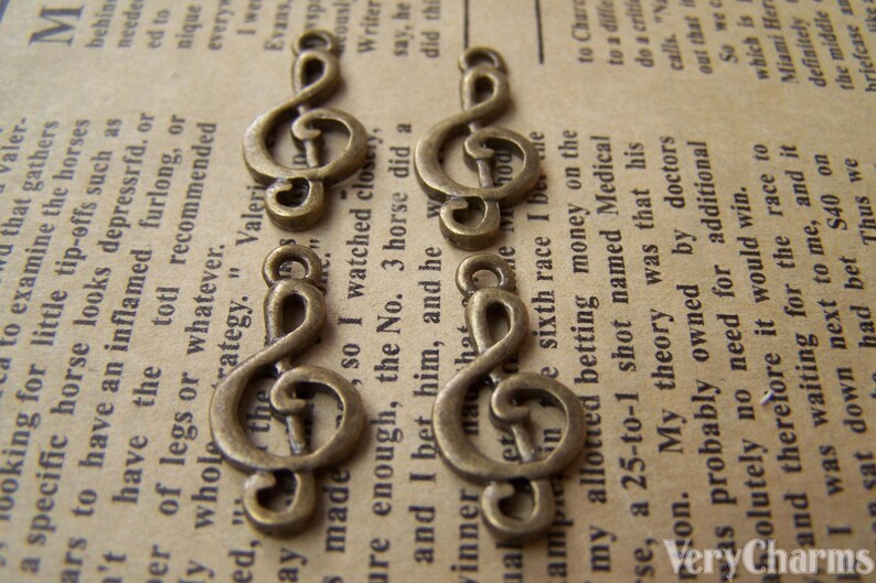 May include: Five antique gold-toned treble clef charms. The charms are arranged in a row on a piece of paper with text.