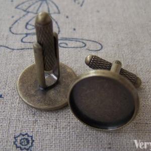 May include: A pair of antique brass cufflinks with round glass cabochon settings. The cufflinks have a textured finish and are designed to hold a small image or design.