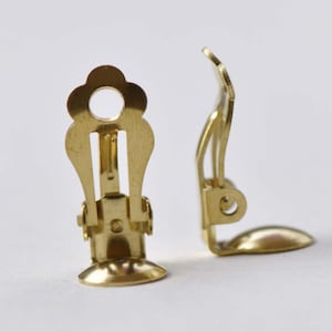 Peut inclure: Une paire de clips d'oreille dorés. Les clips sont en métal et ont un design en forme de fleur. Les clips sont fermés et prêts à être attachés aux boucles d'oreilles.
