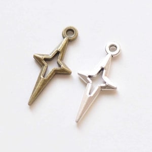 May include: Two star-shaped charms, one bronze-toned and one silver-toned, each with a loop at the top for hanging. The stars have a pointed design with a star-shaped cutout in the center. These charms are ideal for jewelry making or craft projects.