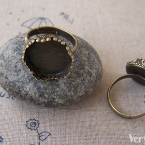 Puede incluir: Dos anillos ajustables de bronce con biseles redondos para agregar un camafeo u otro adorno. Los biseles tienen un borde decorativo.