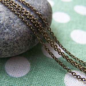 May include: Close-up of a bronze chain necklace on a green and white polka dot fabric background. The chain is made of multiple strands of small, linked rings.