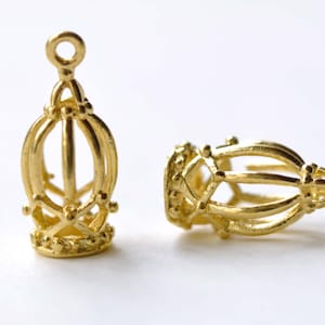 May include: Two gold-colored metal cage-like pendant charms with a loop at the top. The charms are intricately designed with a delicate, openwork pattern.