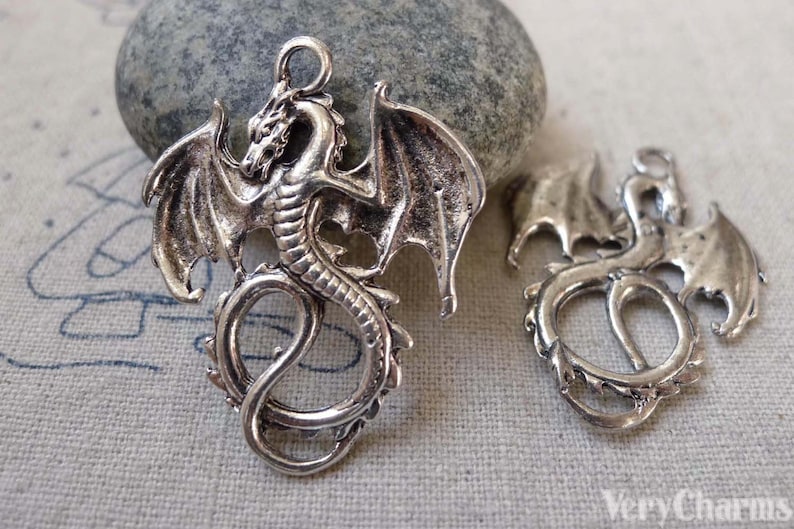 May include: Two silver-toned dragon charms with open wings and curled tails. The charms are detailed with scales and have a loop at the top for attaching to jewellery.