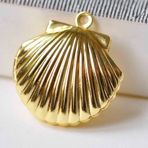 Puede incluir: Un colgante de concha de mar de color dorado con una textura nervada detallada. El colgante tiene un bucle en la parte superior para sujetarlo a un collar o pulsera.