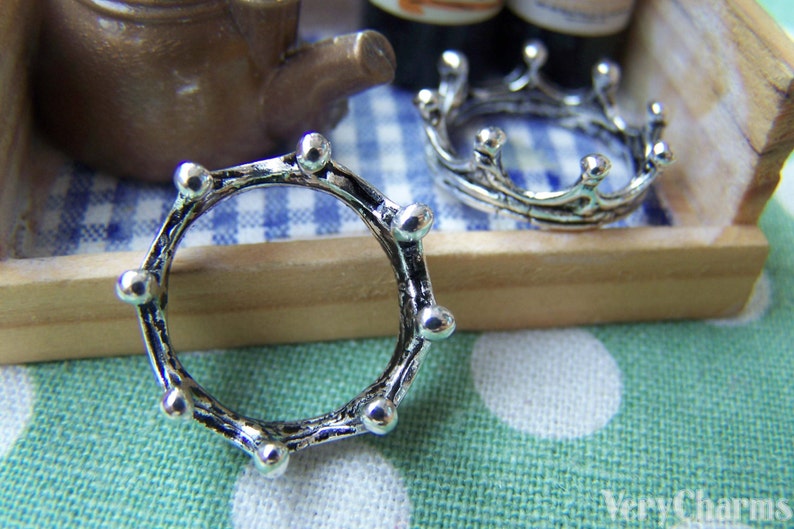 Puede incluir: Dos anillos de plata en forma de corona. El anillo de la izquierda es un c&iacute;rculo simple con una superficie texturizada. El anillo de la derecha tiene un dise&ntilde;o m&aacute;s elaborado con puntos alrededor del c&iacute;rculo.