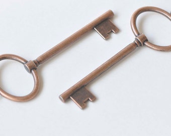May include: Two antique-style keys with a copper finish. One key has a round loop at the top, while the other has a more traditional keyhole shape.