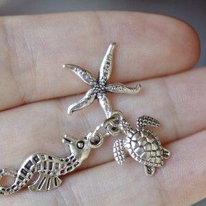K&ouml;nnte beinhalten: Silberner Charm-Set mit einem Seestern, einem Seepferdchen und einer Schildkr&ouml;te. Die Charms sind detailliert und haben einen Vintage-Look.