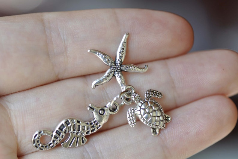 K&ouml;nnte beinhalten: Silberner Charm-Set mit einem Seestern, einem Seepferdchen und einer Schildkr&ouml;te. Die Charms sind detailliert und haben einen Vintage-Look.