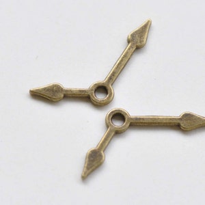 May include: Two antique gold-toned clock hands with pointed tips. The hands are designed for use in a clock or watch.