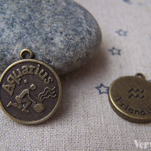 May include: Two bronze-colored metal charms with an Aquarius zodiac sign. The first charm features the word "Aquarius" written around the zodiac symbol. The second charm features the zodiac symbol and the word "Friendly".