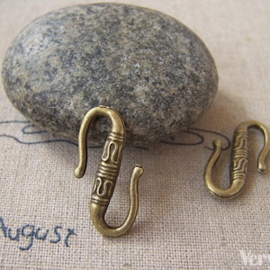 May include: Two antique gold-toned metal hooks with decorative details. The hooks are S-shaped and have a textured design.