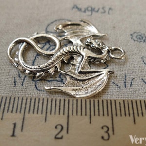 May include: Silver-toned dragon charm with detailed wings and a curled tail. The charm measures approximately 3 cm in length.