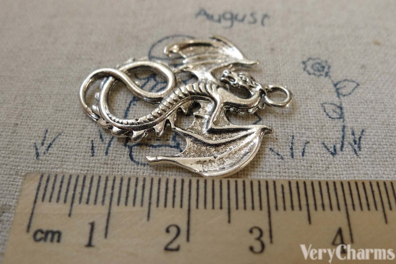 May include: Silver-toned dragon charm with detailed wings and a curled tail. The charm measures approximately 3 cm in length.