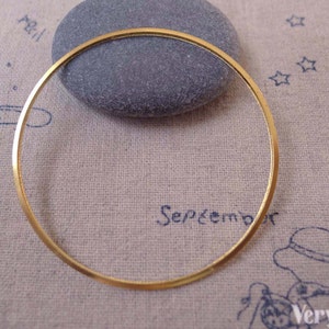 Può includere: Un sottile anello di metallo color oro, forse un componente di gioielleria, è mostrato contro un tessuto strutturato di colore chiaro. Una pietra liscia e grigia è appoggiata dietro l'anello. La parola "September" è visibile sul tessuto.