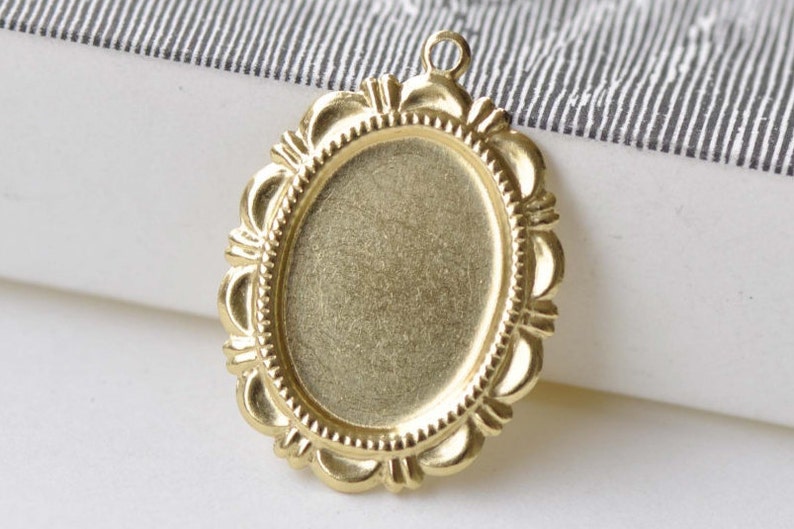 Peut inclure: Pendentif ovale dor&eacute; avec une bordure d&eacute;corative et orn&eacute;e. Le pendentif a une surface lisse et vierge pour ajouter un motif ou une image.