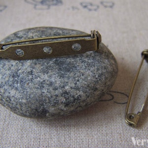 May include: Two antique gold-toned metal safety pin closures. One is a straight pin with a simple design. The other is a bar pin with three holes and a decorative end.