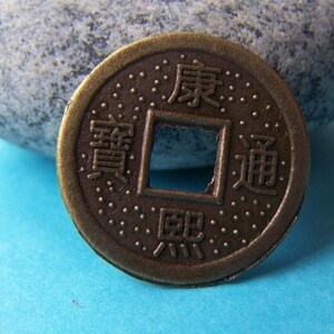 K&ouml;nnte beinhalten: Eine bronzene chinesische M&uuml;nze mit einem quadratischen Loch in der Mitte. Die M&uuml;nze tr&auml;gt chinesische Schriftzeichen, darunter "Wohlstand" und "Gl&uuml;ck".